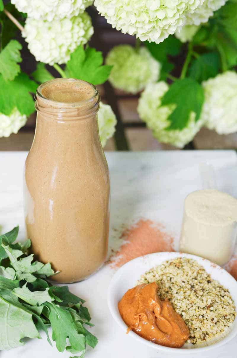 Botella de batido vegano de proteína de mantequilla de maní rodeado de todos los ingredientes crudos 