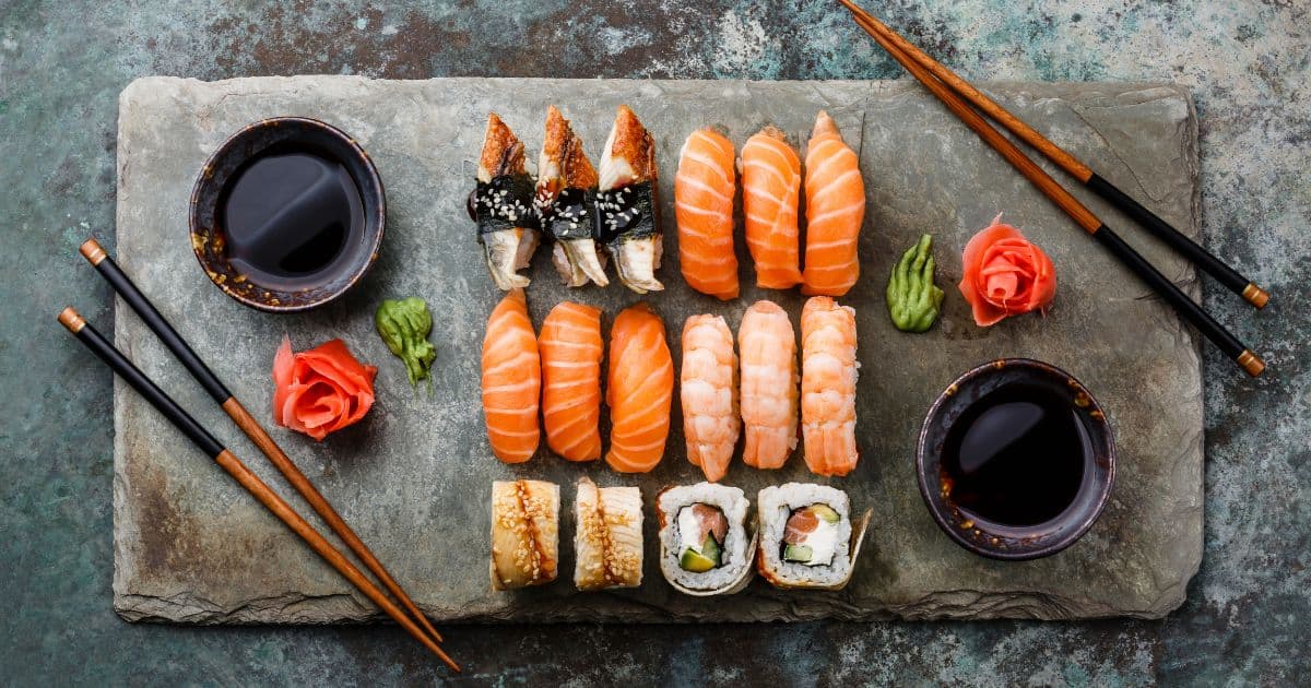 Fuente con una variedad de rollos de sushi, palitos chinos y un plato de salsa